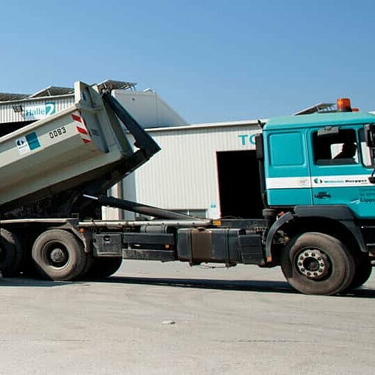 Zwei Männer stehen vor einem LKW, der einen Container neben viele weitere Container absetzt.