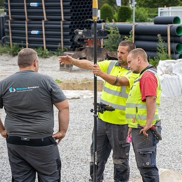 Drei Personen besprechen sich auf einer Baustelle.